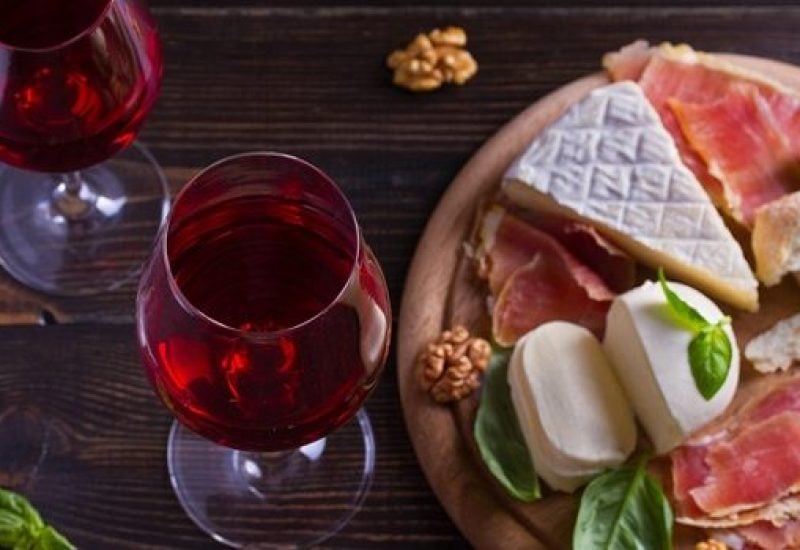 Glasses and bottle of wine with cheese, bread, nuts and jamon or prosciutto on dark wooden background