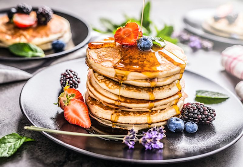 Pancakes with strawberries blackberries blueberries lavender mint leaves and maple syrup.