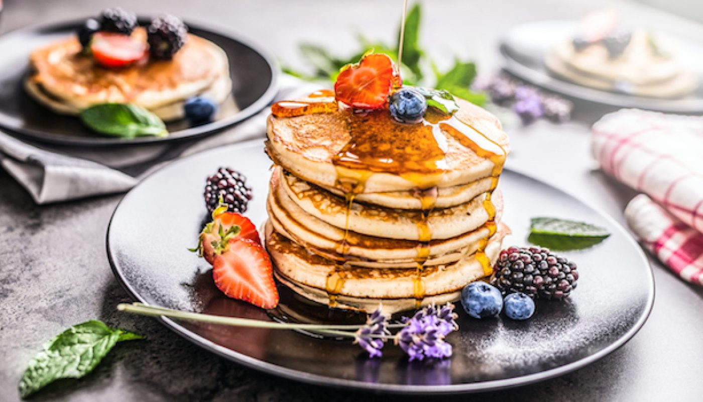 Pancakes with strawberries blackberries blueberries lavender mint leaves and maple syrup.