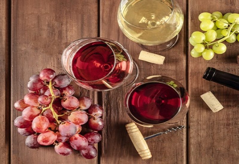 Retro Cellar Wine Tasting. A photo of glasses of red, rose, and white wine with a bottle, grapes, and a vintage corkscew and corks, shot from the top on a dark rustic wooden background with copy space