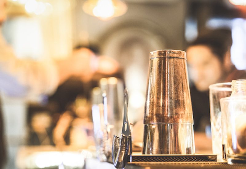 Blurred defocused side view of barman preparing drink to guest at speakeasy cocktail bar - Social gathering concept with people enjoying time together - Warm vintage filter with focus on shaker