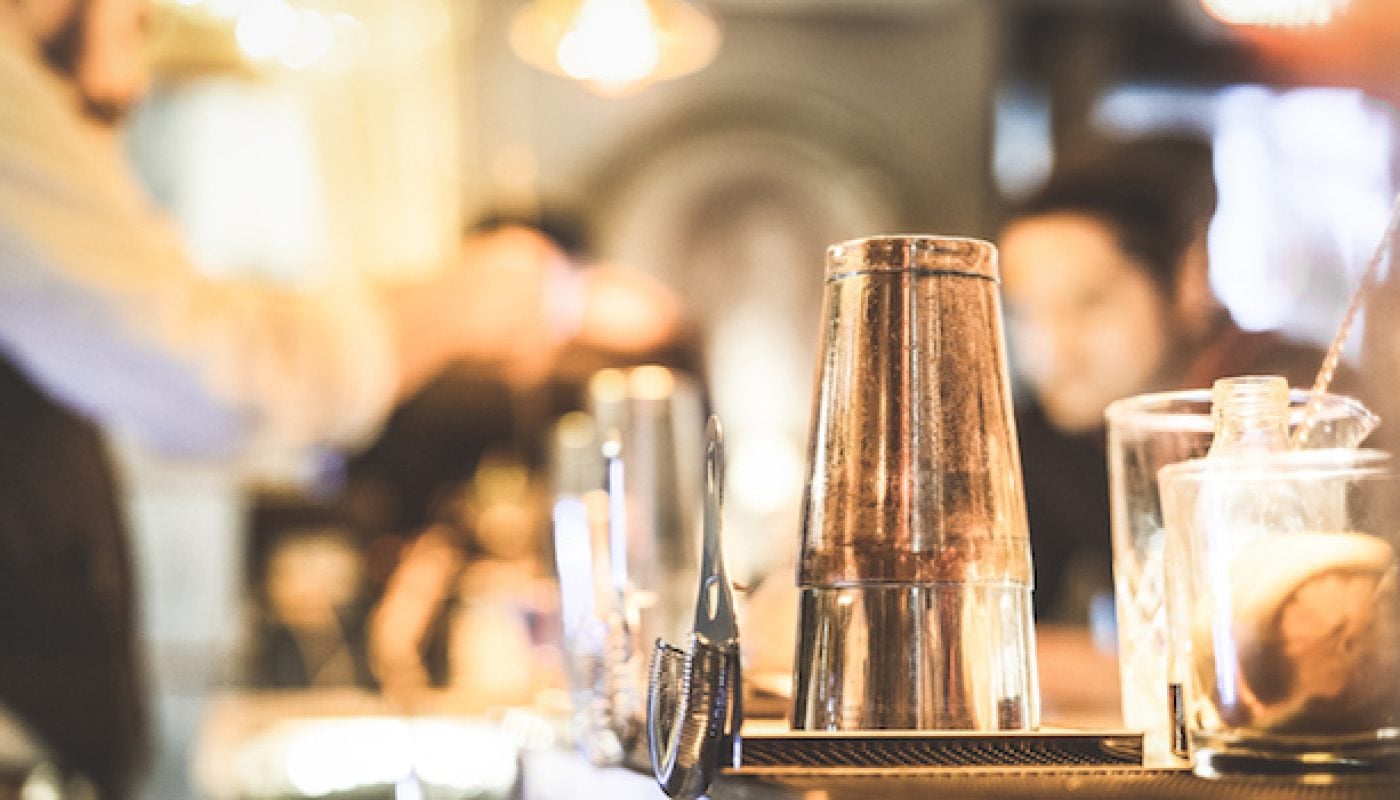 Blurred defocused side view of barman preparing drink to guest at speakeasy cocktail bar - Social gathering concept with people enjoying time together - Warm vintage filter with focus on shaker