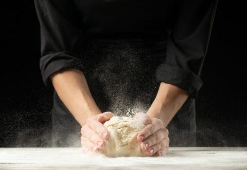 Bakery. Man preparing the bread, Easter cake, Easter bread or cross buns on a wooden table in the bakery close up. Cook preparing bread dough.