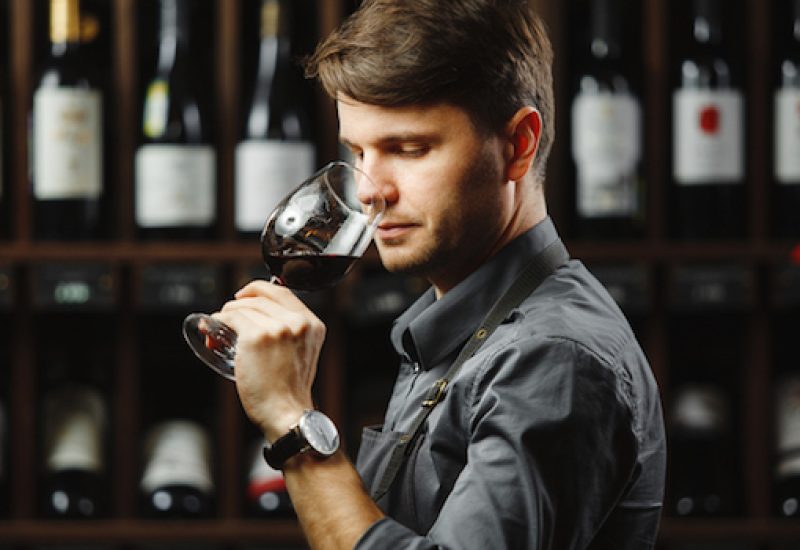 Bokal of red wine on background, male sommelier appreciating drink
