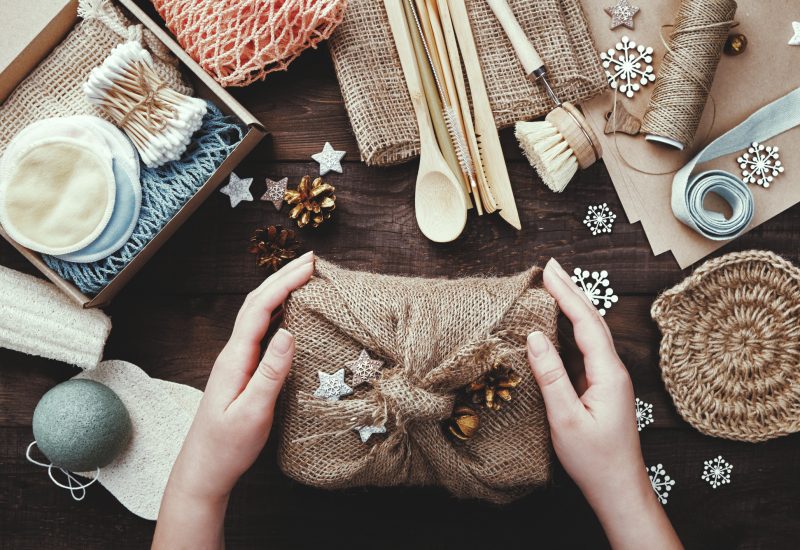Zero waste christmas. Female hands hold gift wrapped in burlap. Eco friendly products laid out on table