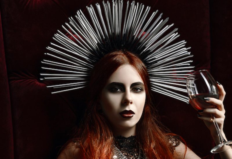 Gothic fashion: young woman sitting in chair and holding glass