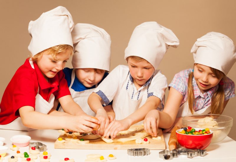 Four cute bakers, boys and girl in cook's uniform having fun making candy filled cookies