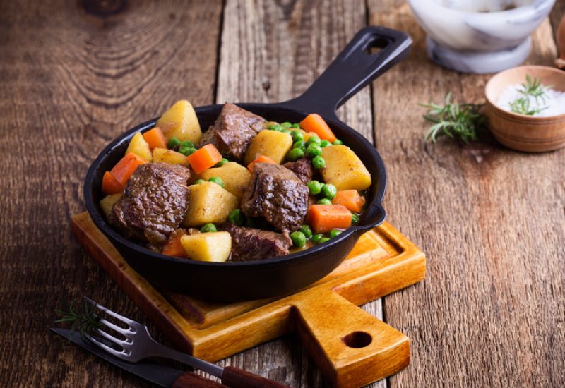 Beef and vegetable stew with potatoes in cast iron skillet on rural table