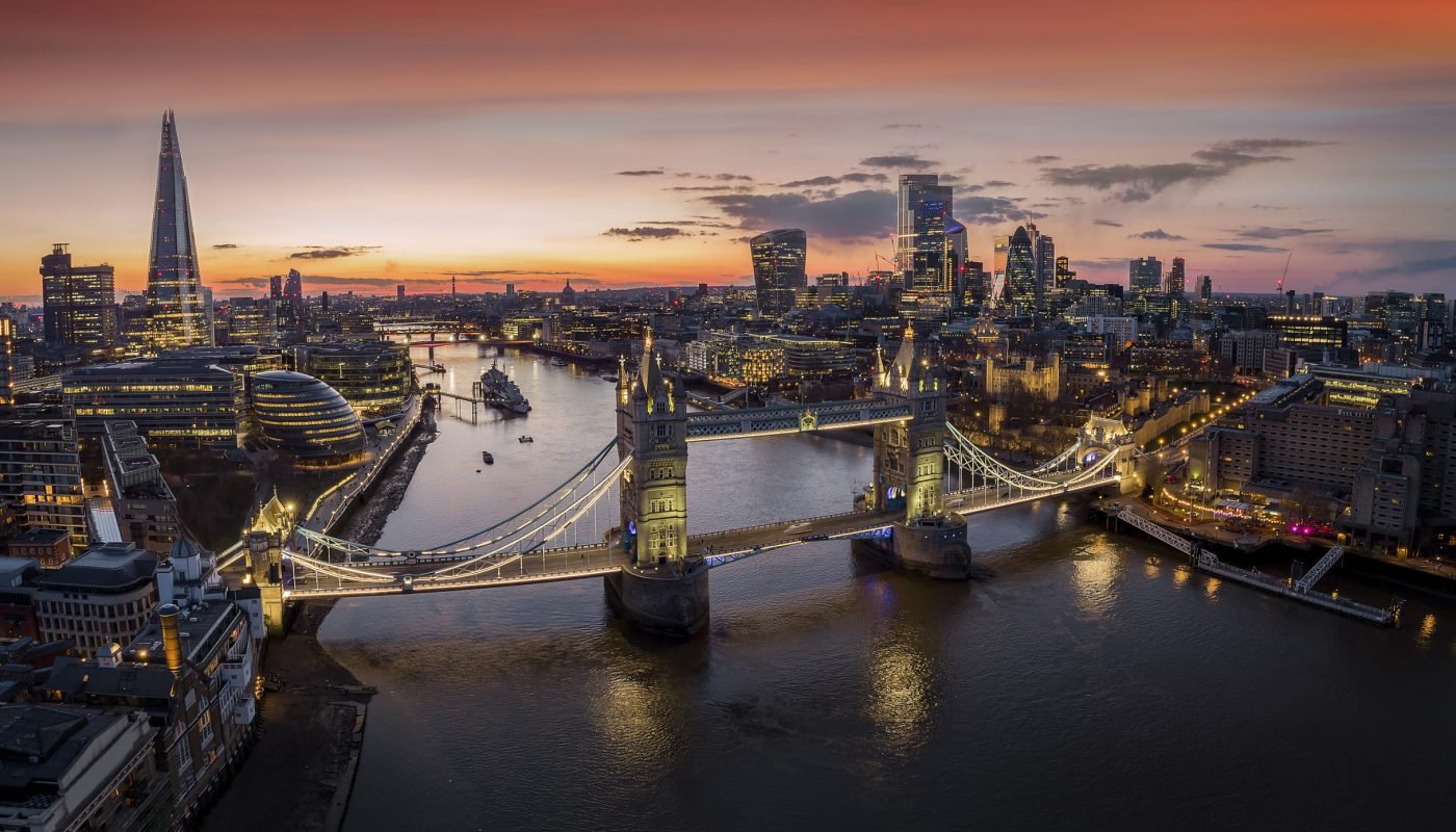 Panoramic, aerial view to the cityscape of London with Tower Bridge and the illuminated skyscrapers of the city during dusk, United Kingdom