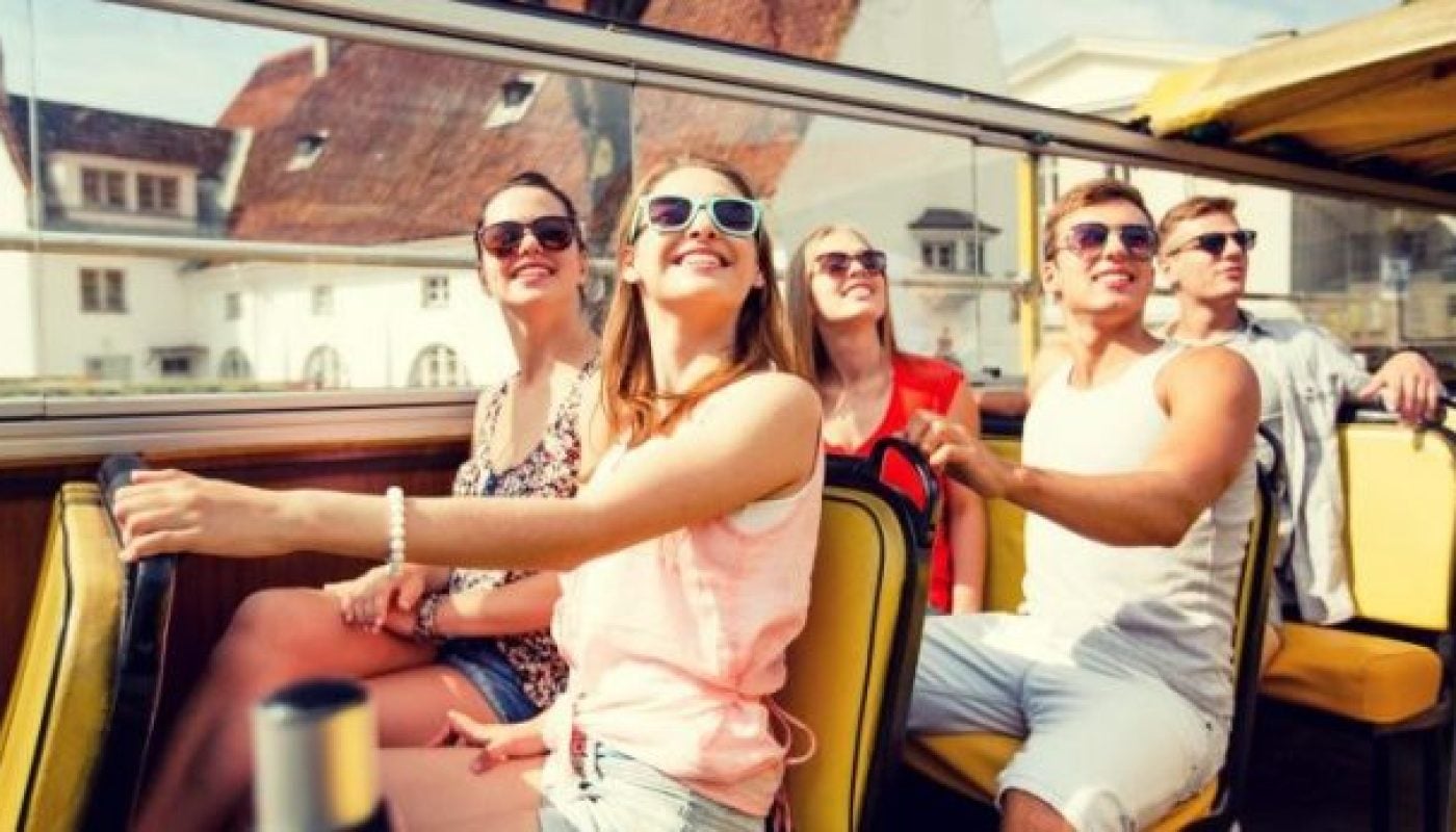 group of smiling friends traveling by tour bus