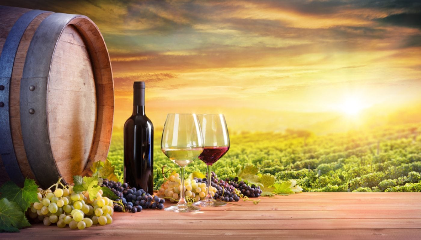 Wine Glasses And Bottle With Barrel In Vineyard At Sunset
