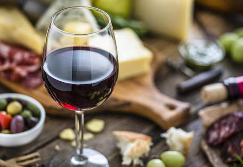 Appetizer: red wineglass, cheese and spanish chorizo on rustic wooden table